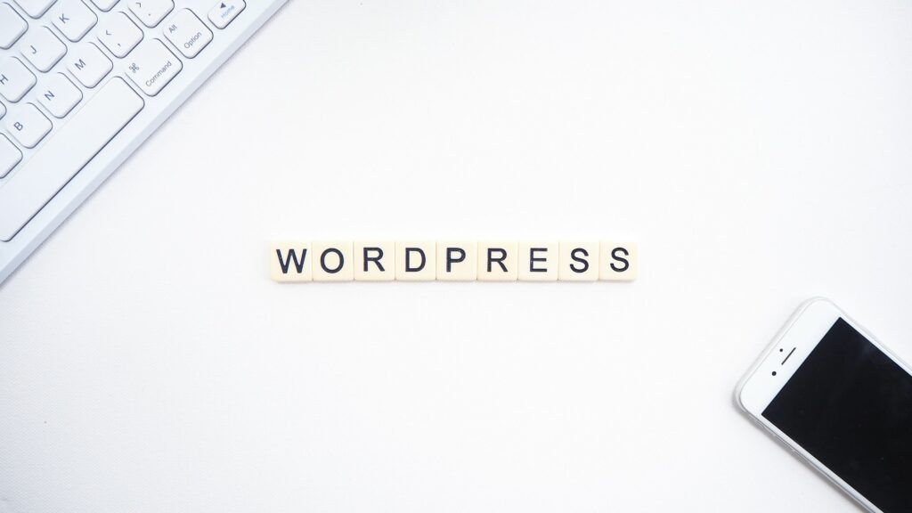 weiße oberfläche, das wort wordpress klein im zentrum, am rand eine tastatur und ein handy zu sehen. bild zum beitrag: Was ist der Unterschied zwischen Wordpress.org und wordpres.com